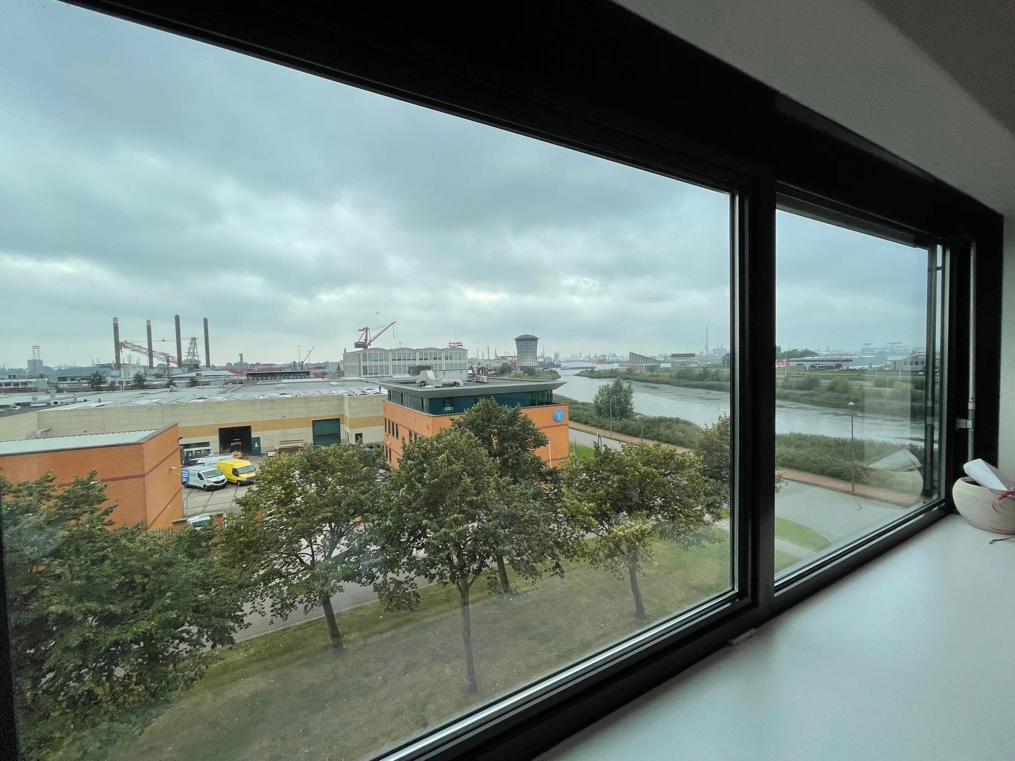 Uitzicht vanuit een raam op de Karel Doormanweg met industrieterrein, water en gebouwen op een bewolkte dag.